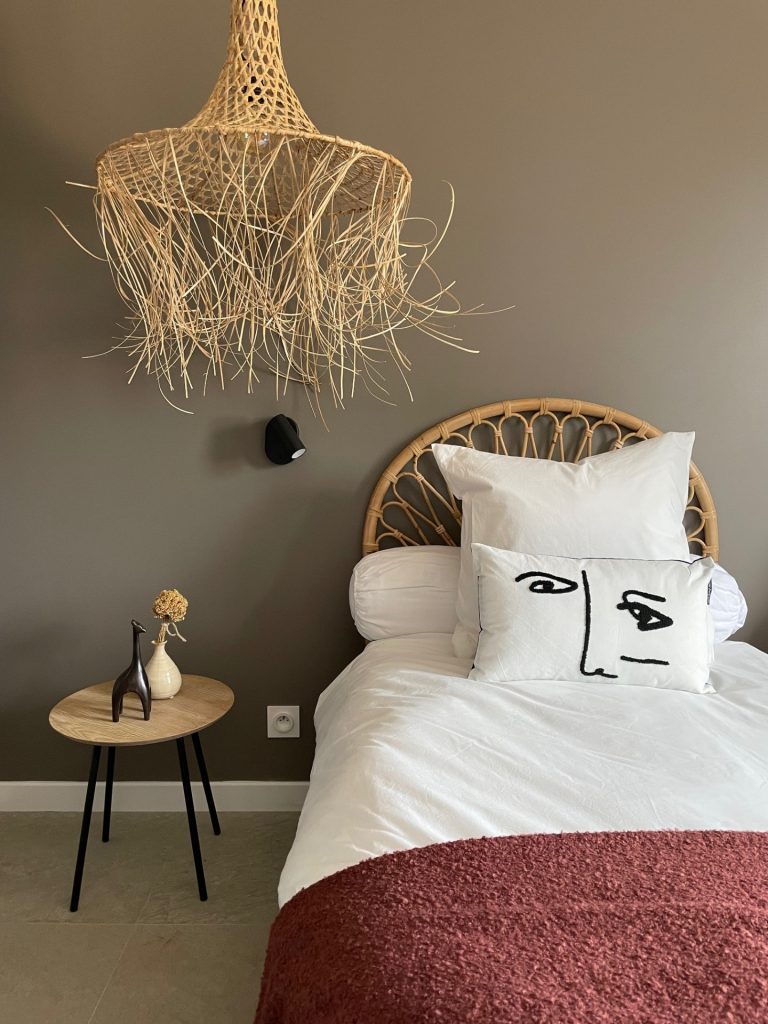 Chambre agrémentée de suspensions en osier tressé, dans des tons sombres et chaleureux, créant une ambiance naturelle et apaisante.