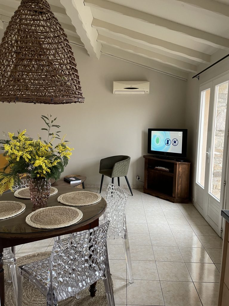 Salle à manger décorée avec table ronde et vue sur la télévision en fond, ambiance conviviale et moderne du projet de home staging A Casa Cantone en Corse.