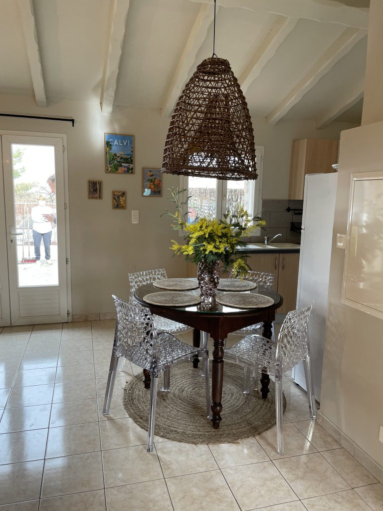 Salle à manger décorée avec table ronde, chaises transparentes et suspension artisanale, home staging A Casa Cantone Corse.