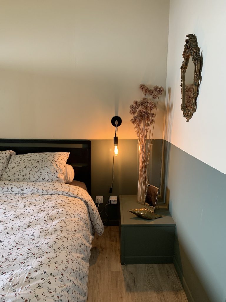 Chambre aux tonalités apaisantes de vert kaki et de beige, avec des détails noirs ajoutant une touche de contraste subtil pour une ambiance sereine et relaxante.