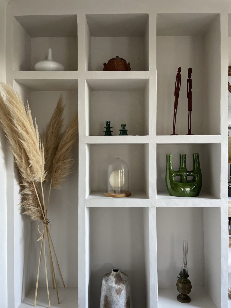 Bibliothèque murale à la chaux avec niches décoratives, objets d'art, vases, plantes vertes, créant une ambiance élégante et épurée.