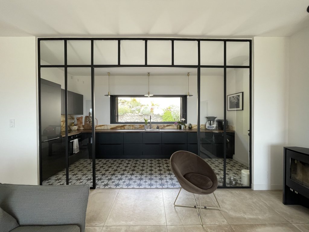 Vue depuis le salon sur la cuisine, avec une séparation élégante en verrière industrielle créant une démarcation subtile entre les deux espaces.