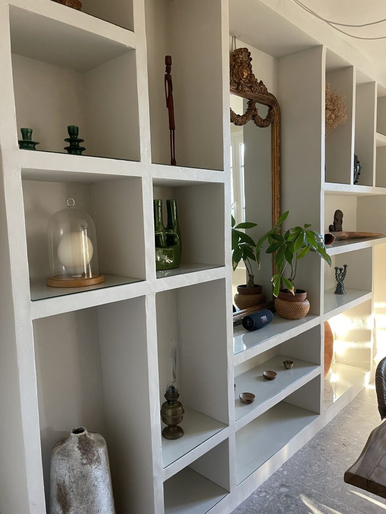 Bibliothèque en chaux avec niches, objets artisanaux, vases et miroirs, pour un design raffiné et méditerranéen.