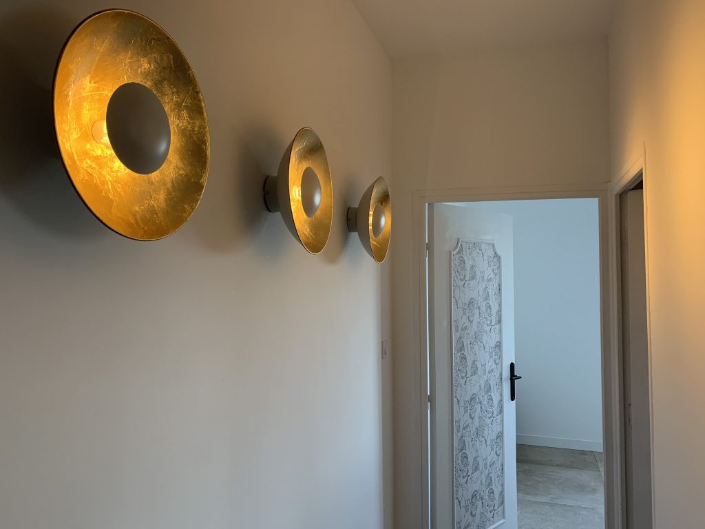 Enfilade d'appliques lumineuses dans le couloir menant aux chambres, créant une ambiance chaleureuse et accueillante.