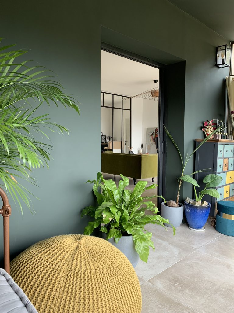 Véranda traitée en tonalité de kaki, avec murs et plafond harmonieux, créant une atmosphère chaleureuse et immersive, semblable à un jardin d'hiver.