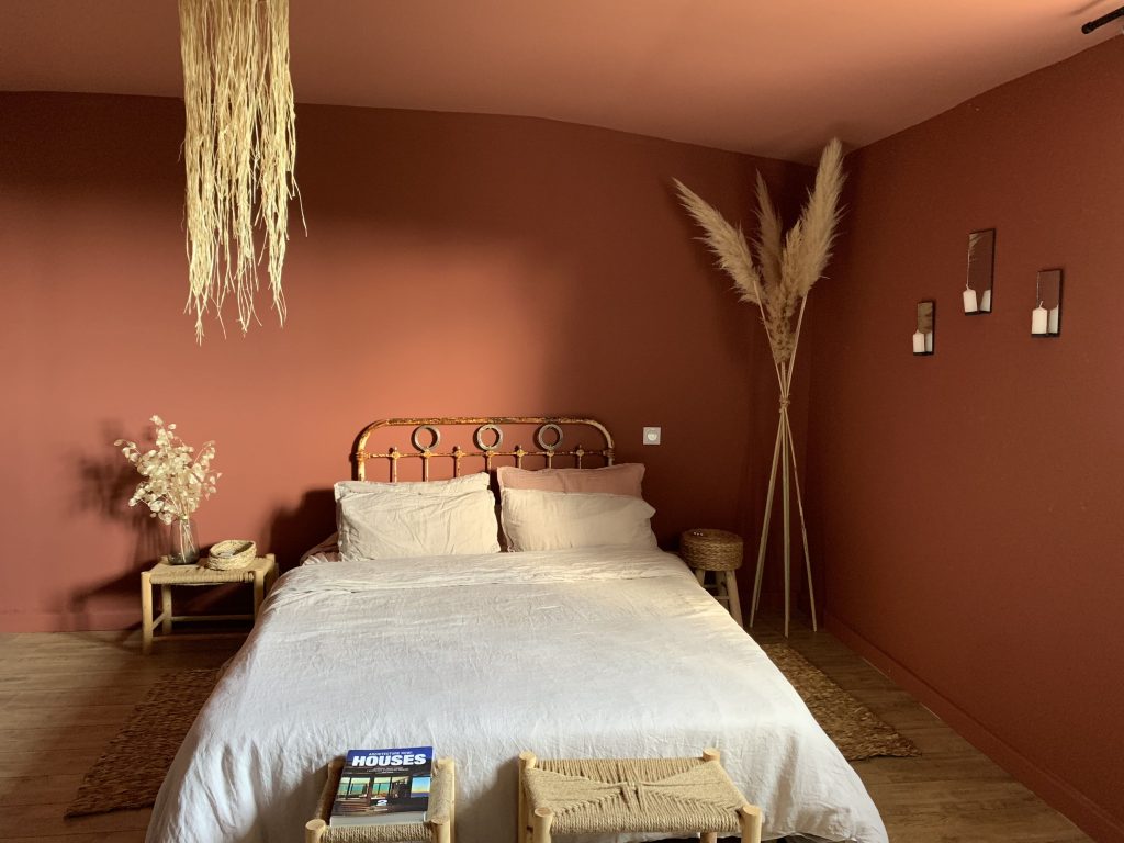 Chambre de la suite parentale, cocon chaleureux et douillet avec des murs et un plafond au tonalités terracotta, parquet massif au sol, literie en lin et éléments en cannage créant une ambiance intime et apaisante.