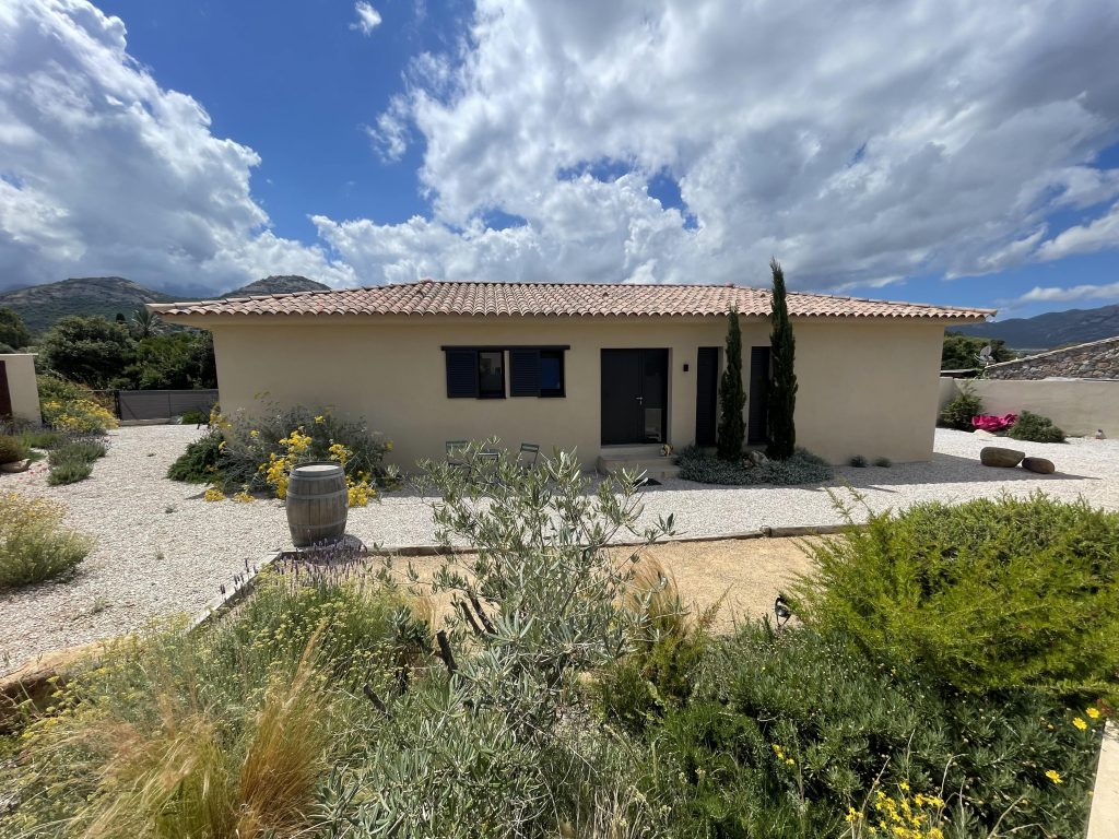 Vue d'ensemble de La Villa Geneviève, villa rectangulaire avec une toiture 4 pentes de style méditerranéen avec des lignes contemporaines, menuiseries élégantes et entourée d'une végétation typique de la Corse, près de Calvi.