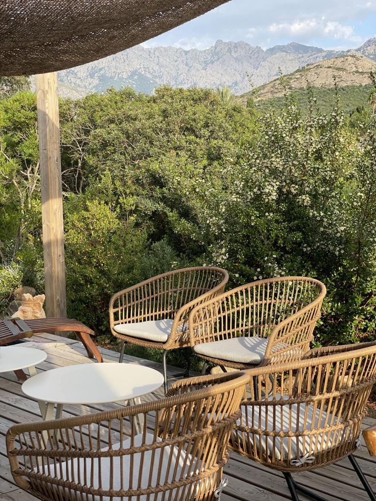 Terrasse de La Villa Geneviève avec un salon extérieur abrité par une toile d'ombrage en fibre de coco, offrant une vue sur la maquis et les montagnes de Calvi au départ du GR20.