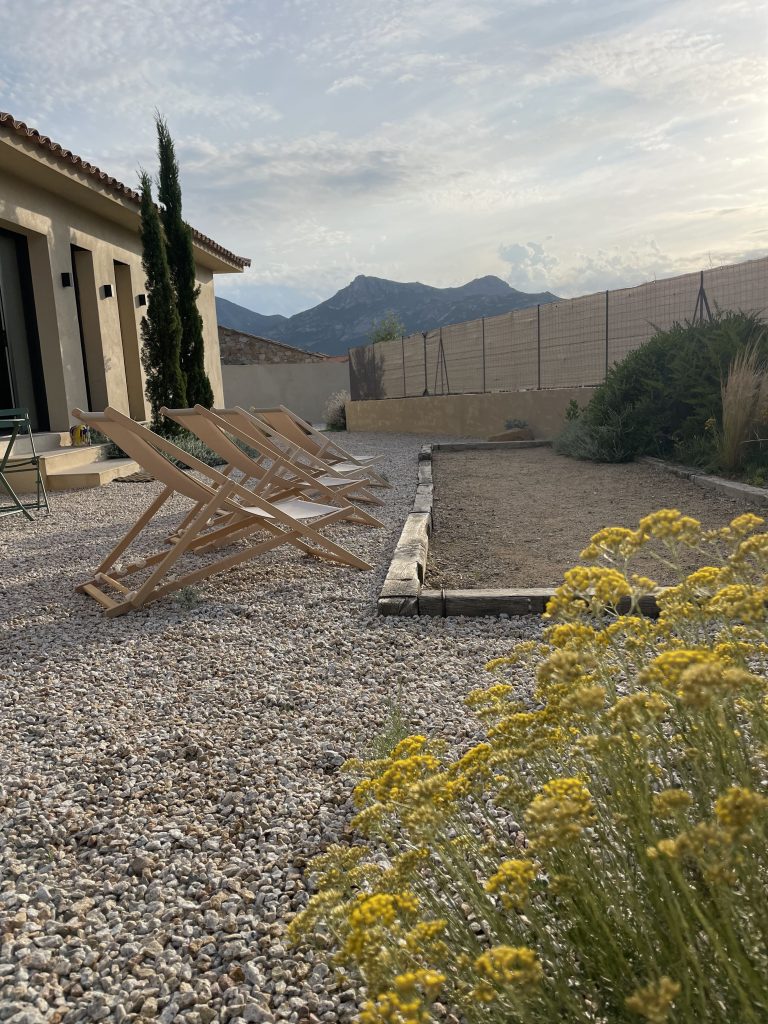 Entrée du jardin de la Villa Geneviève, avec un terrain de pétanque à l'avant-plan et un ensemble de chaises chiliennes colorées.