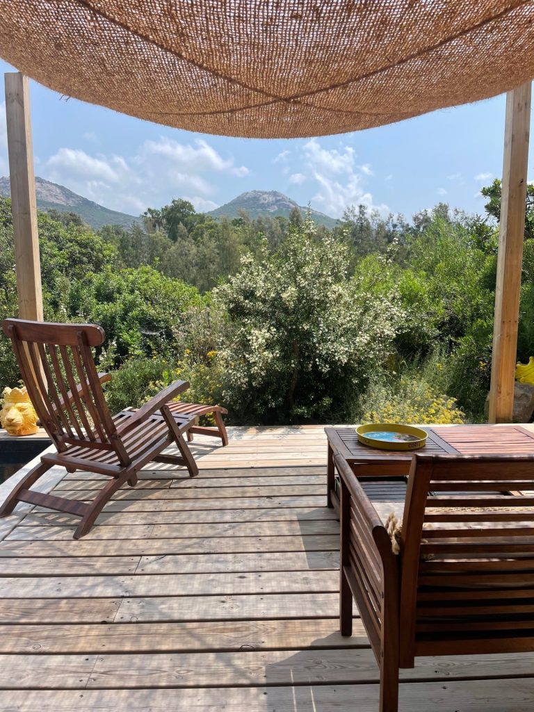 Terrasse de La Villa Geneviève avec un salon extérieur abrité par une toile d'ombrage en fibre de coco, offrant une vue sur la maquis et les montagnes de Calvi au départ du GR20.