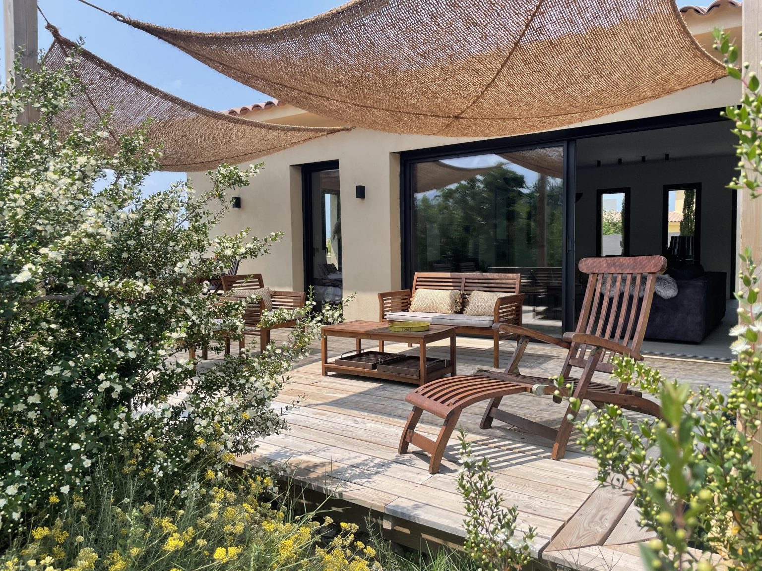 Terrasse extérieure du projet La Villa Geneviève, avec salon cosy ombragé par des voiles d'ombrage en fibre de coco, entourée par la nature et le maquis corse, offrant un espace chaleureux et apaisant pour profiter de l'extérieur.
