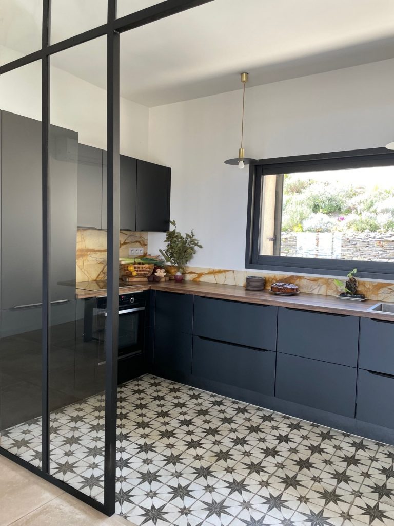 Cuisine contemporaine avec meubles noirs mattes, plans de travail en noyer et crédence en marbre de Sienne mis en valeur par le grand panoramique ouvert sur la nature environnante.