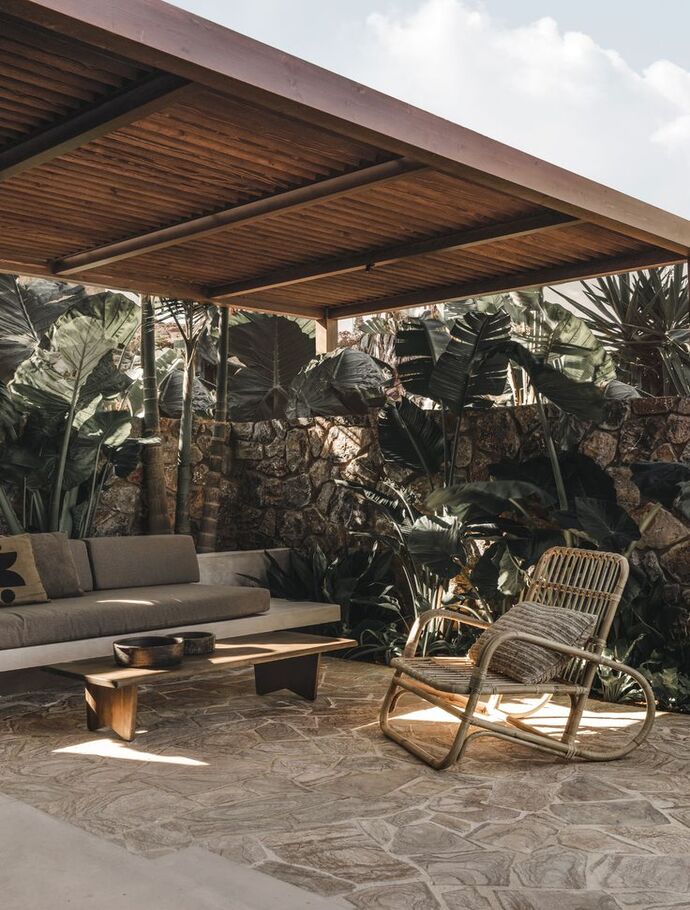 Terrasse extérieure couverte par une pergola en bois aménagée dans un style méditerranéen Le seul empire claire s'harmonise avec un mur en Pierre naturelle, créant une ambiance chaleureuse et authentique