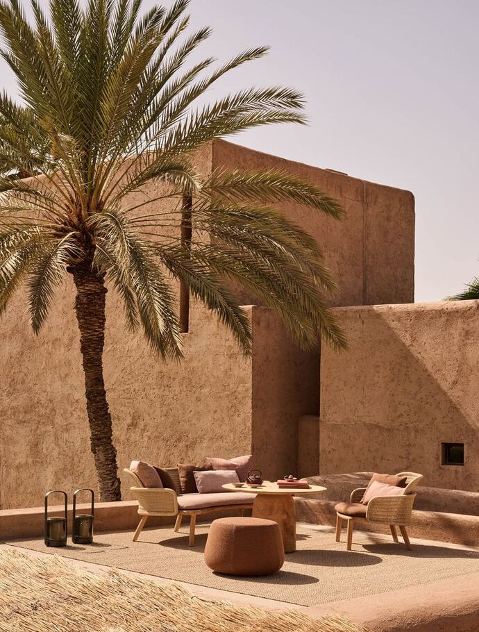 Aménagement extérieur dans un jardin marocain à l'ombre d'un palmier majestueux, les tonalités de terre typique du Maroc créent une atmosphère chaleureuse et apaisante